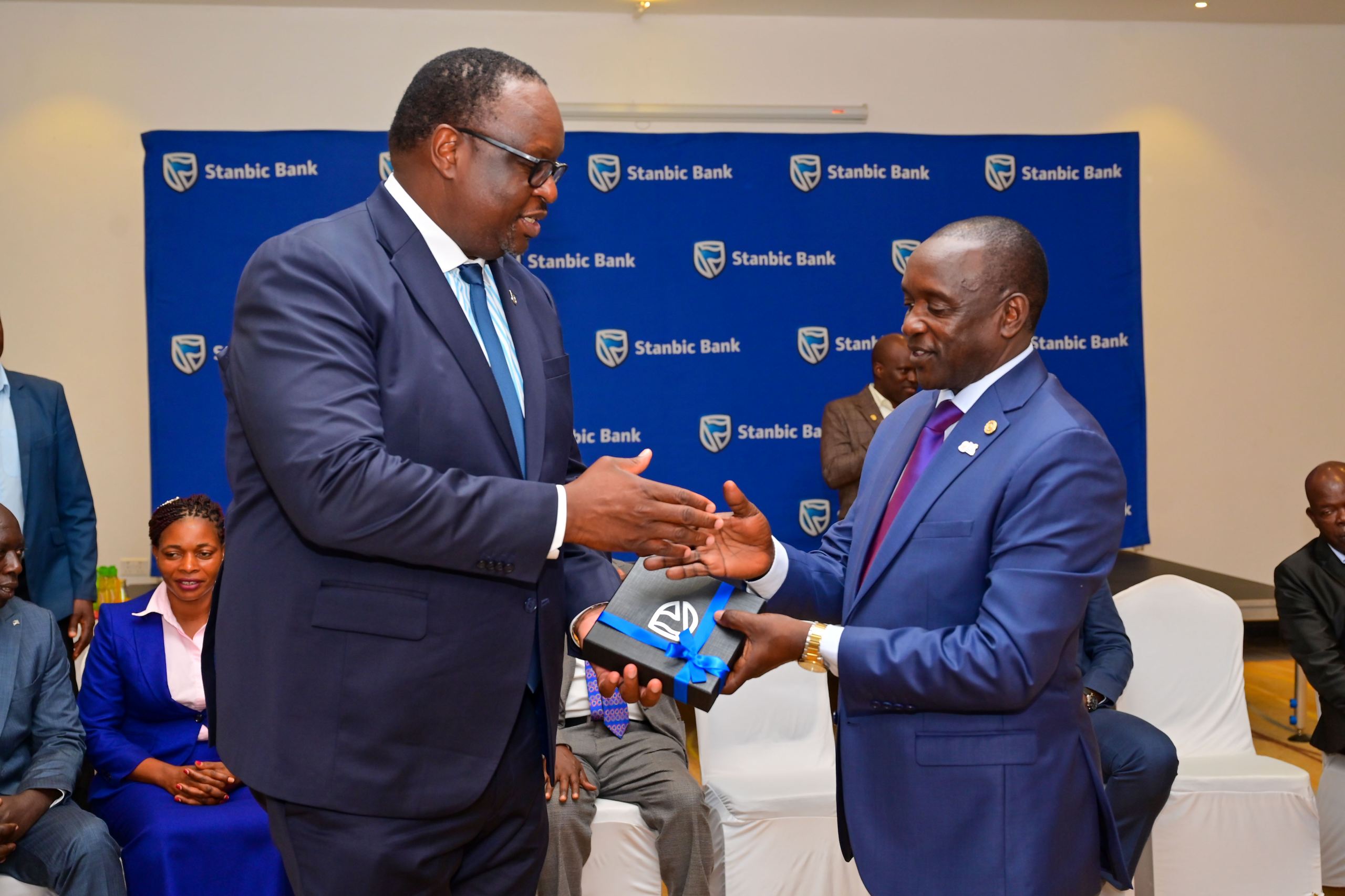 Fred Badda (R), the Resident District Commissioner and current Chairperson of the Kalangala Palm Oil Growers Trust receives a gift from Mumba Kalifungwa the Chief Executive Stanbic Bank Uganda Fred Badda (R), the Resident District Commissioner and current Chairperson of the Kalangala Palm Oil Growers Trust receives a gift from Mumba Kalifungwa the Chief Executive Stanbic Bank Uganda